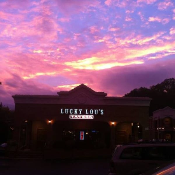 Lucky Lou's Tavern exterior at dusk, with a vibrant pink and purple sunset sky.
