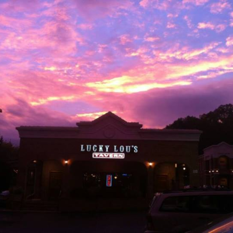 Lucky Lou's Tavern exterior at dusk, with a vibrant pink and purple sunset sky.