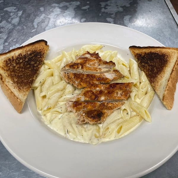 Grilled chicken over penne pasta in cream sauce with two pieces of toasted bread.