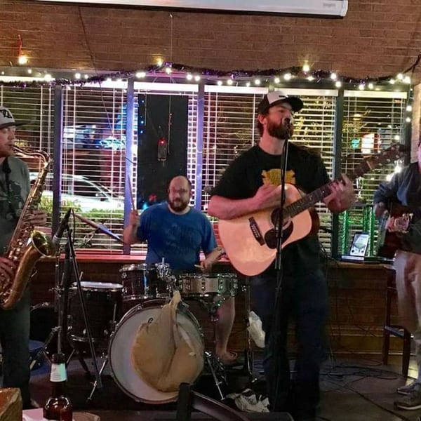 A band performs live at Lucky Lou's Tavern, featuring a guitarist, drummer, and saxophonist.