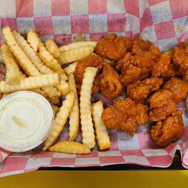 A basket of Lucky Lou's boneless wings in buffalo sauce with crinkle-cut fries and ranch.