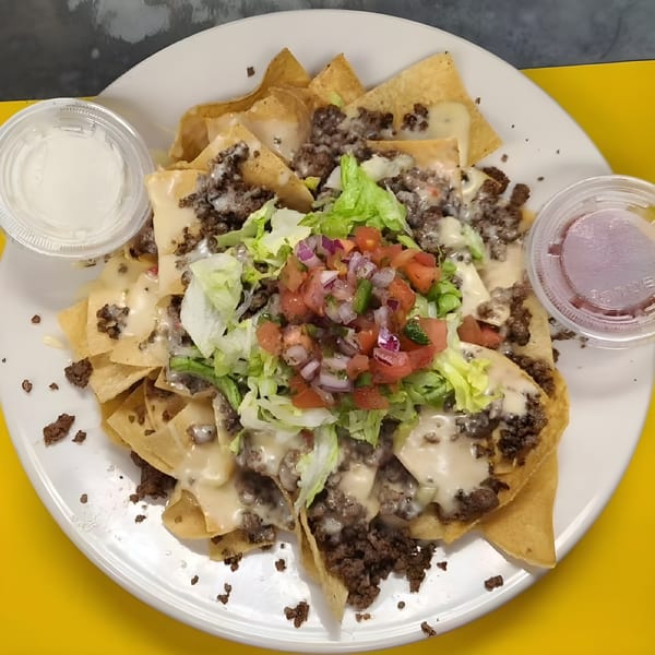 A plate of Lucky Lou's Tavern nachos with ground beef, cheese sauce, lettuce, pico de gallo, and sides.